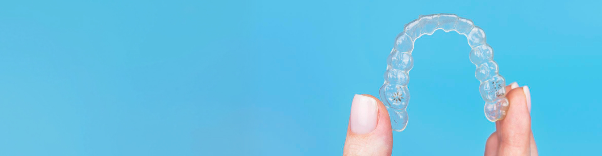 Fingers holding clear aligner.